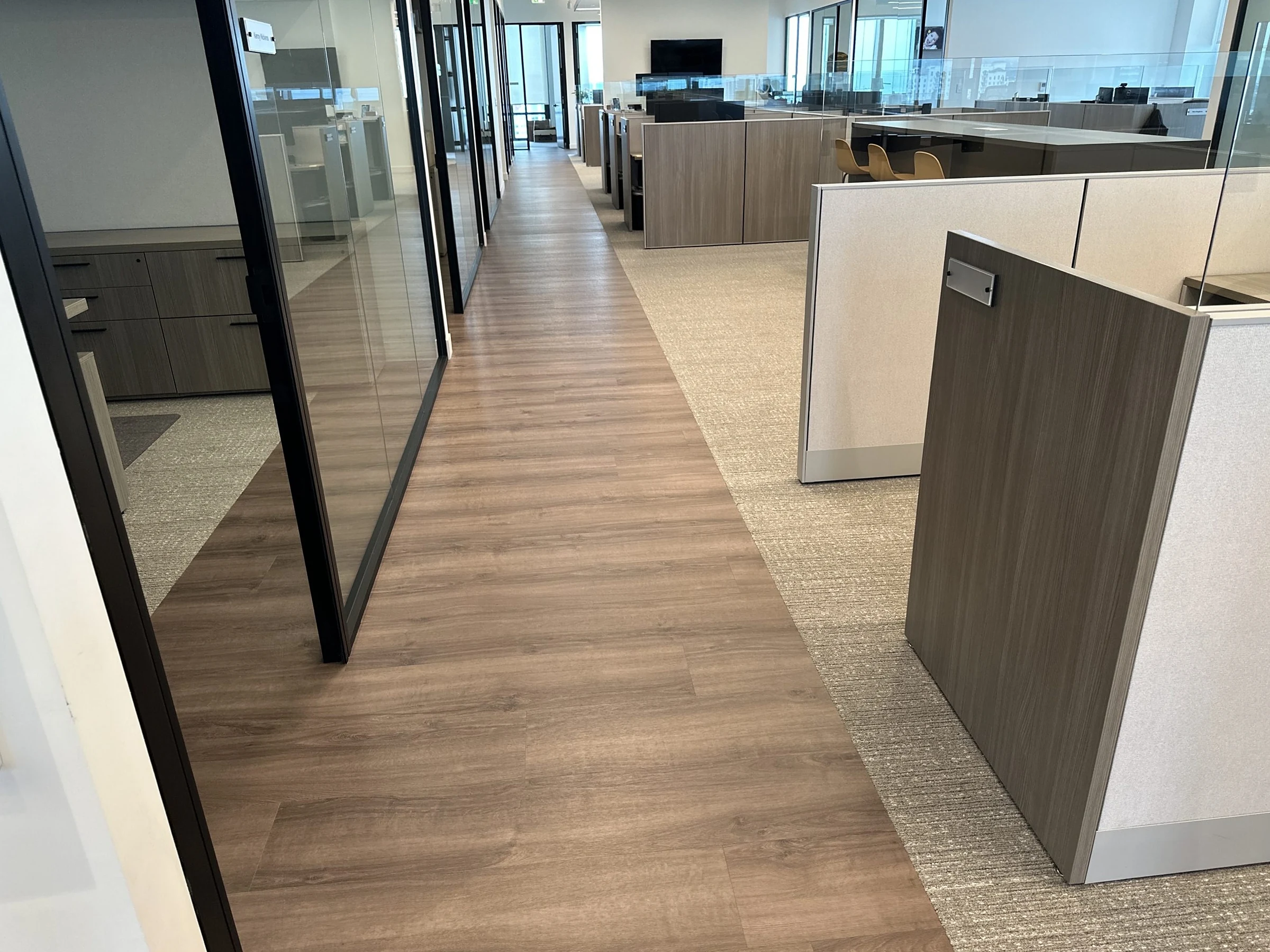 Un pasillo de tablón entre oficinas de vidrio y estaciones de trabajo