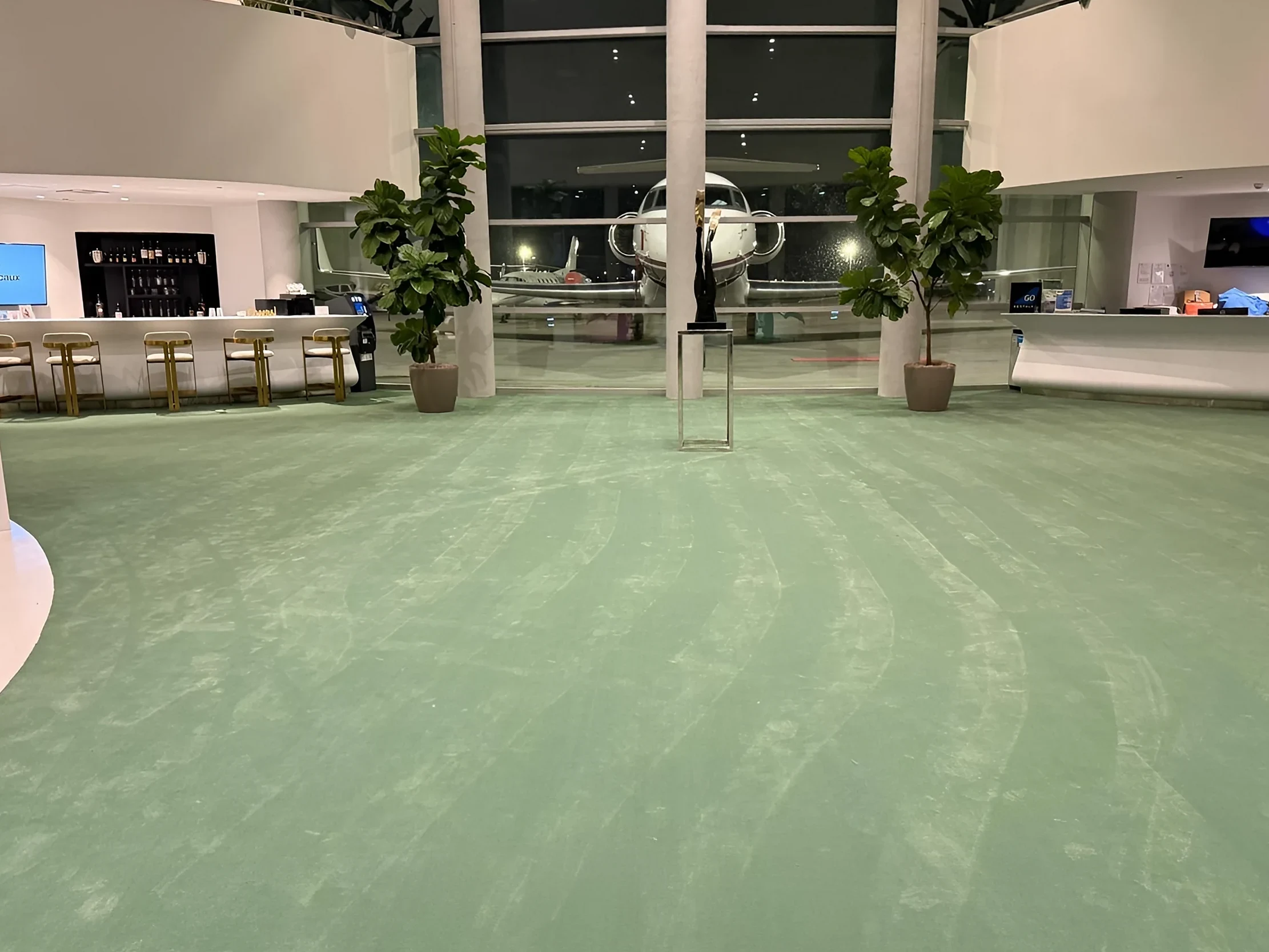 New green broadloom carpet across the Embassair terminal lobby at night, with a private jet parked outside the glass