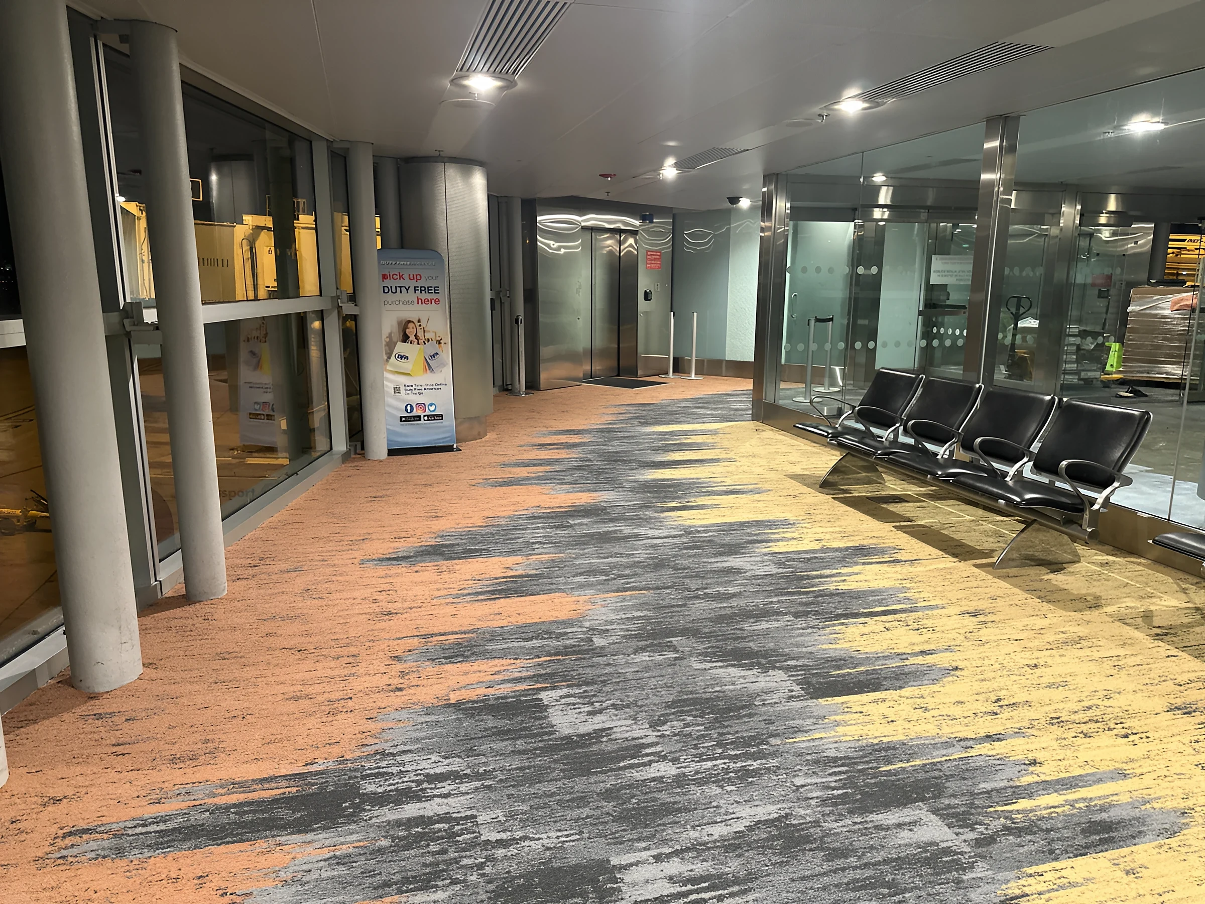 Coral and sun-yellow waves breaking across the grey carpet field in Concourse J
